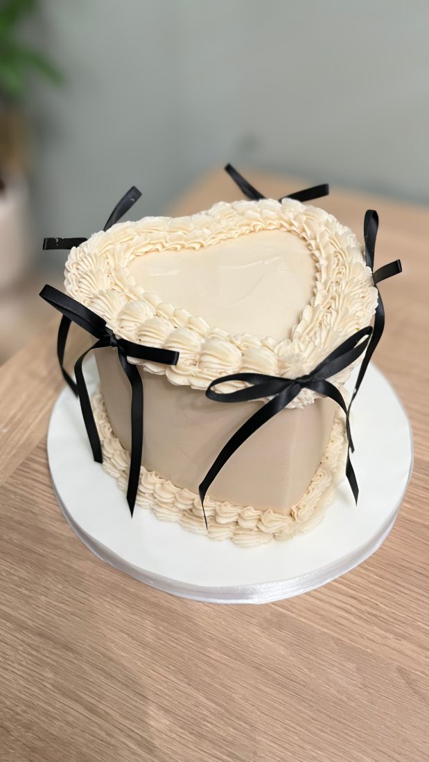Cream heart-shaped cake with piped ruffles and black satin bows