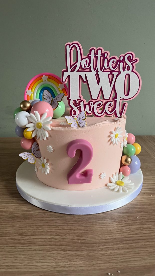 Pink buttercream first birthday cake with daisies and a rainbow topper